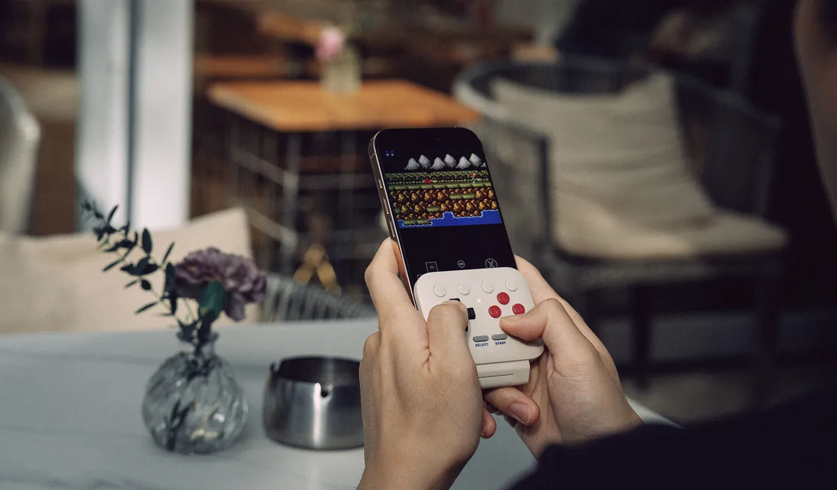 White 8BitDo FlipPad plugged into the USB-C port of a phone, playing a retro game in portrait mode