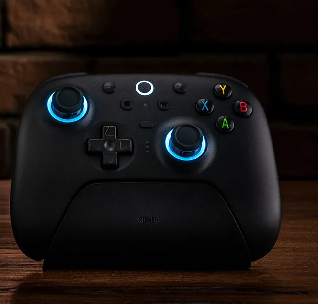 The 8BitDo Ultimate 2 Wireless controller in black, standing in its charging dock with blue light rings around both sticks