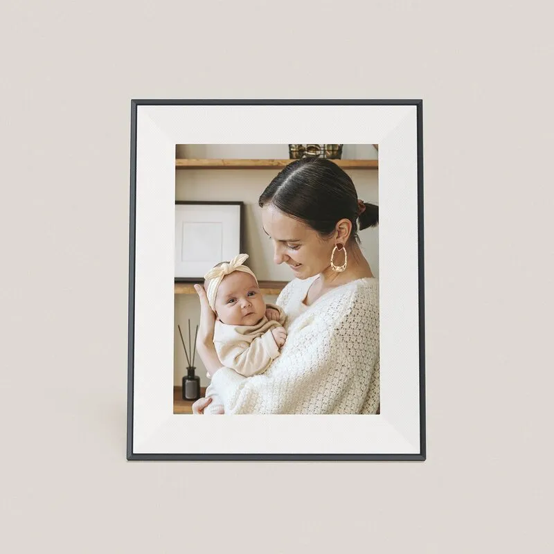 Aura Aspen digital photo frame in Ink with a white mat, standing upright and showing a photo of a mother holding a baby