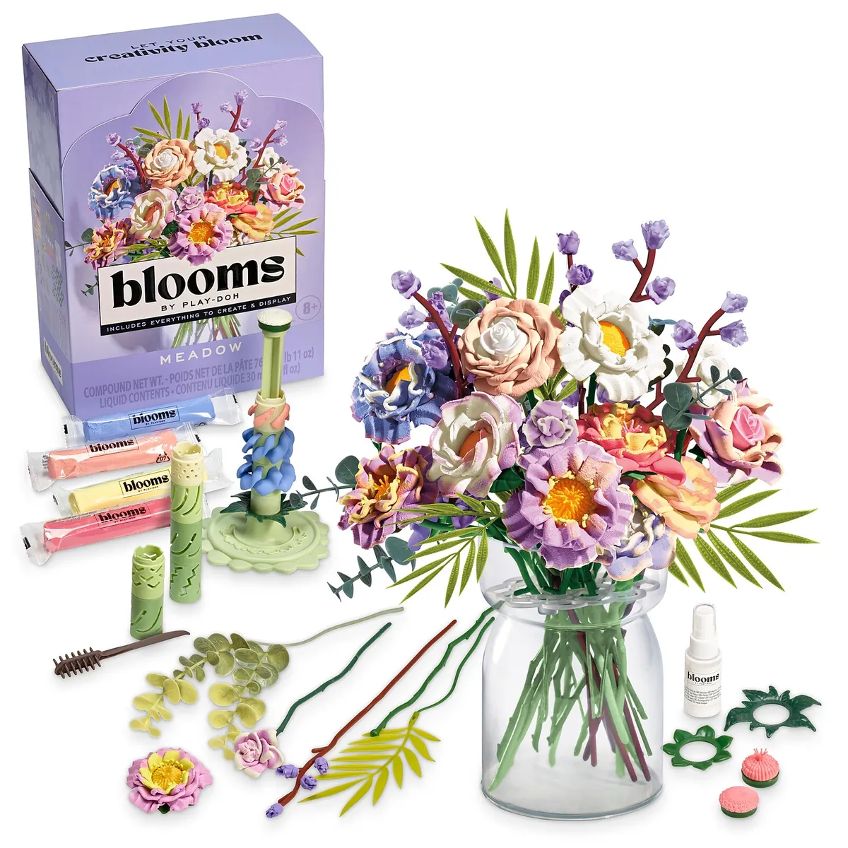 Blooms by Play-Doh Meadow kit box next to a finished pastel bouquet in a clear vase, with the dough sticks and tools in front