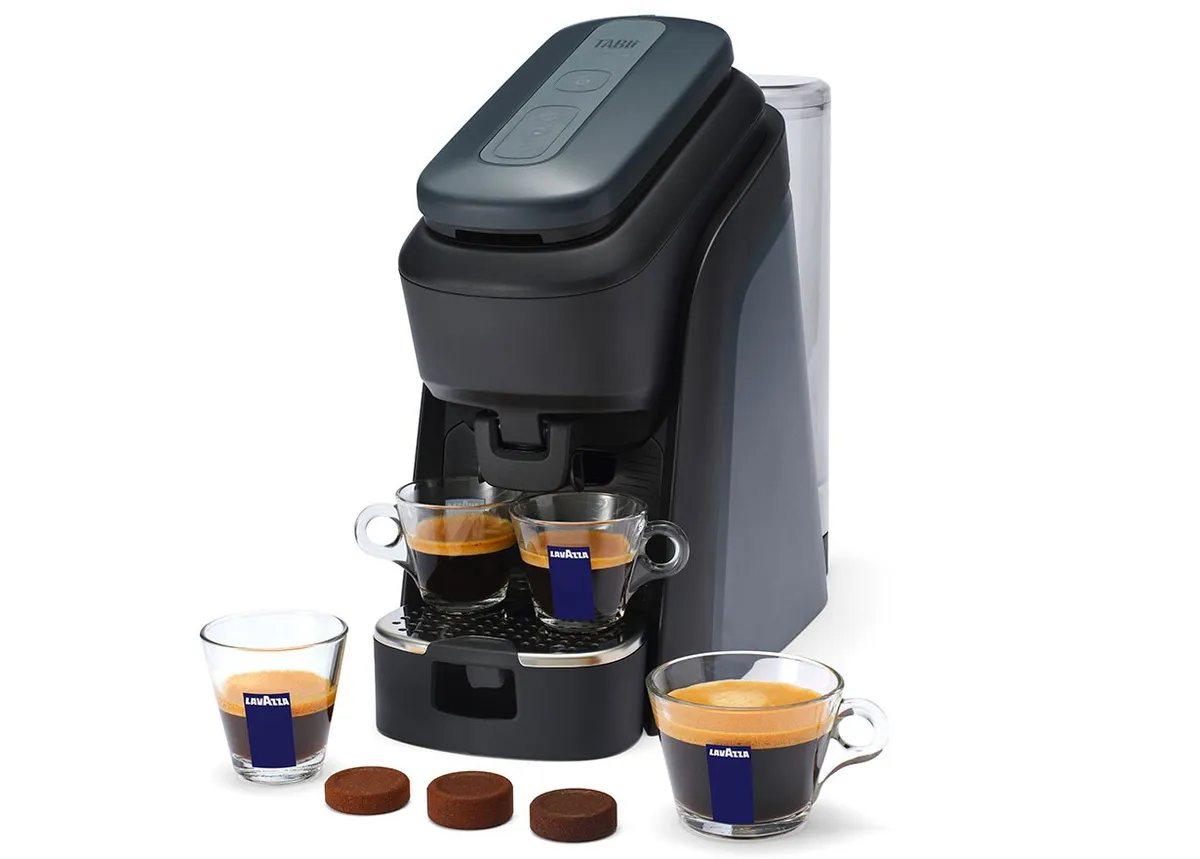 Black Lavazza Tablì espresso machine with two espresso glasses under the spout and three round coffee tabs in front