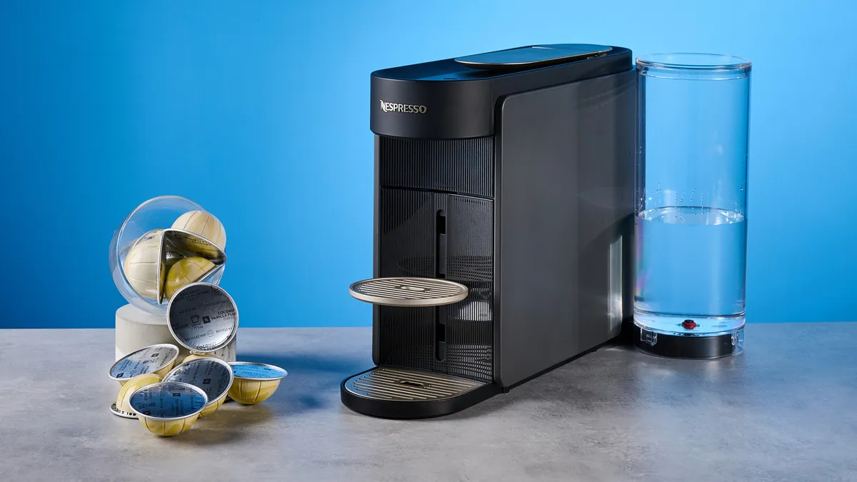 Black Nespresso Vertuo Up pod coffee machine with a glass water tank and a pile of Vertuo pods