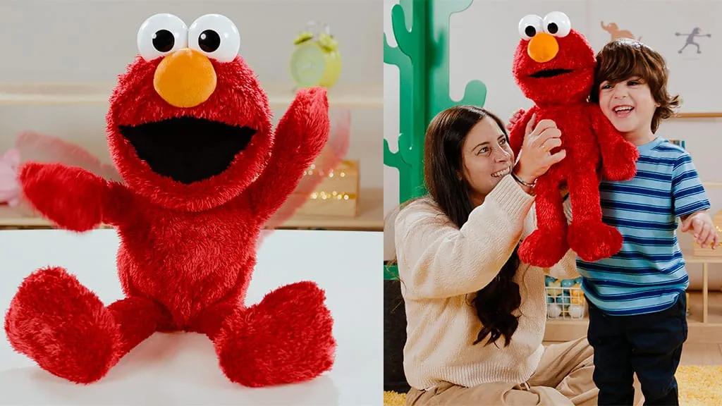 Tickle Me Elmo Giggle Max plush with his arms raised, sitting on a white table